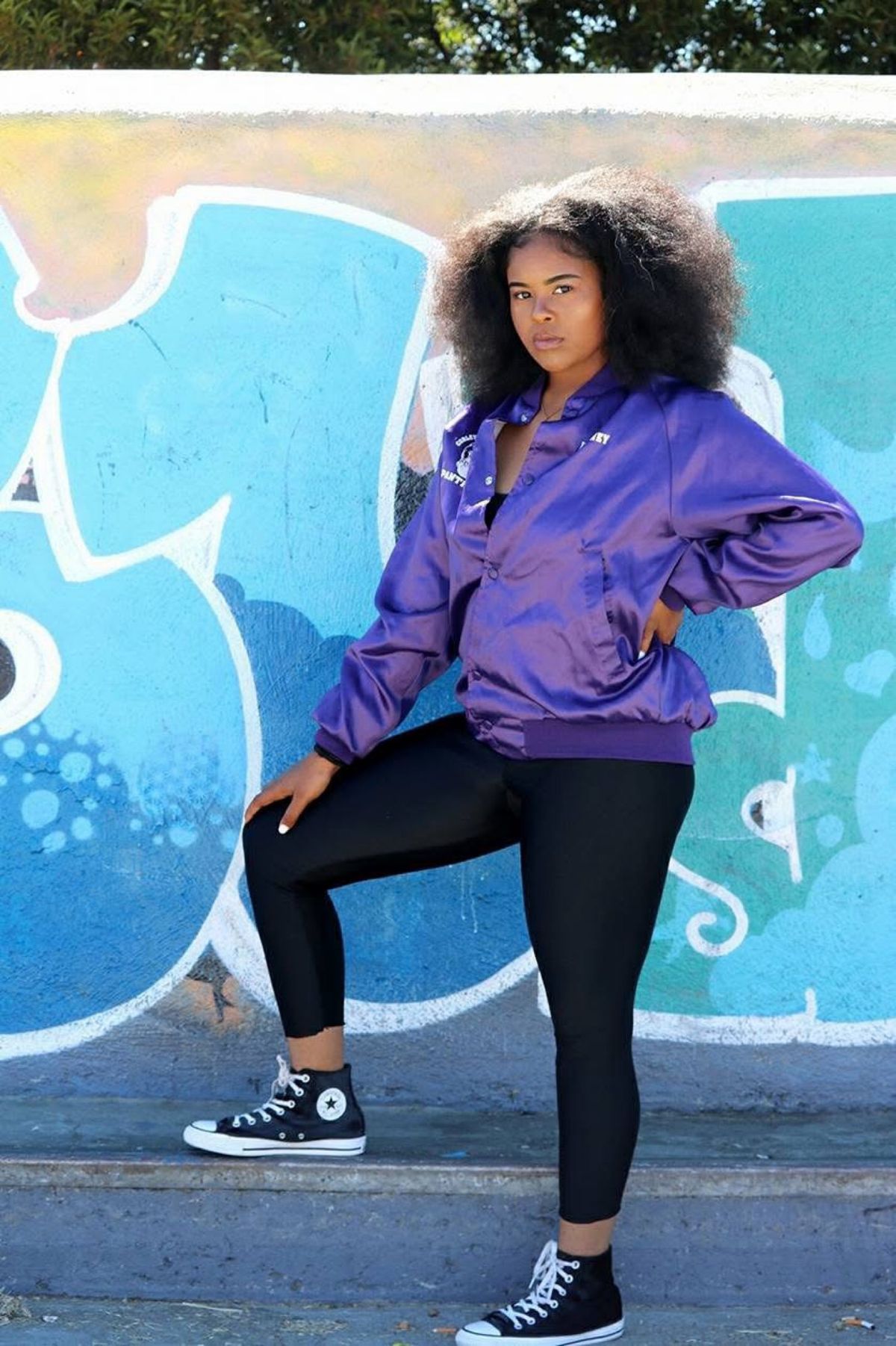 Dejah Vú in a purple satin jacket in front of a blue mural